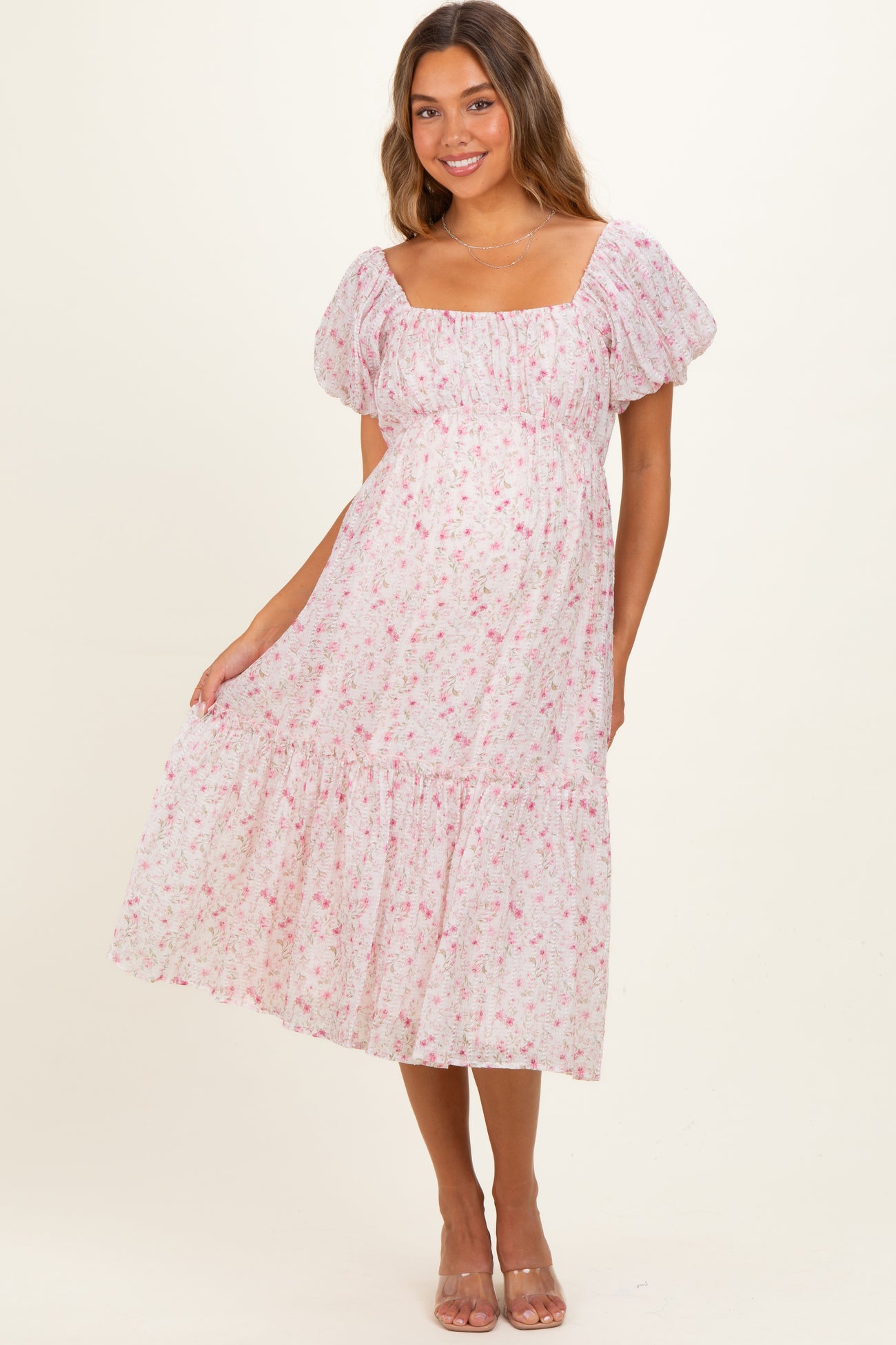 woman wearing a pink floral maternity maxi dress with puff sleeves and tiered skirt, showing her baby bump