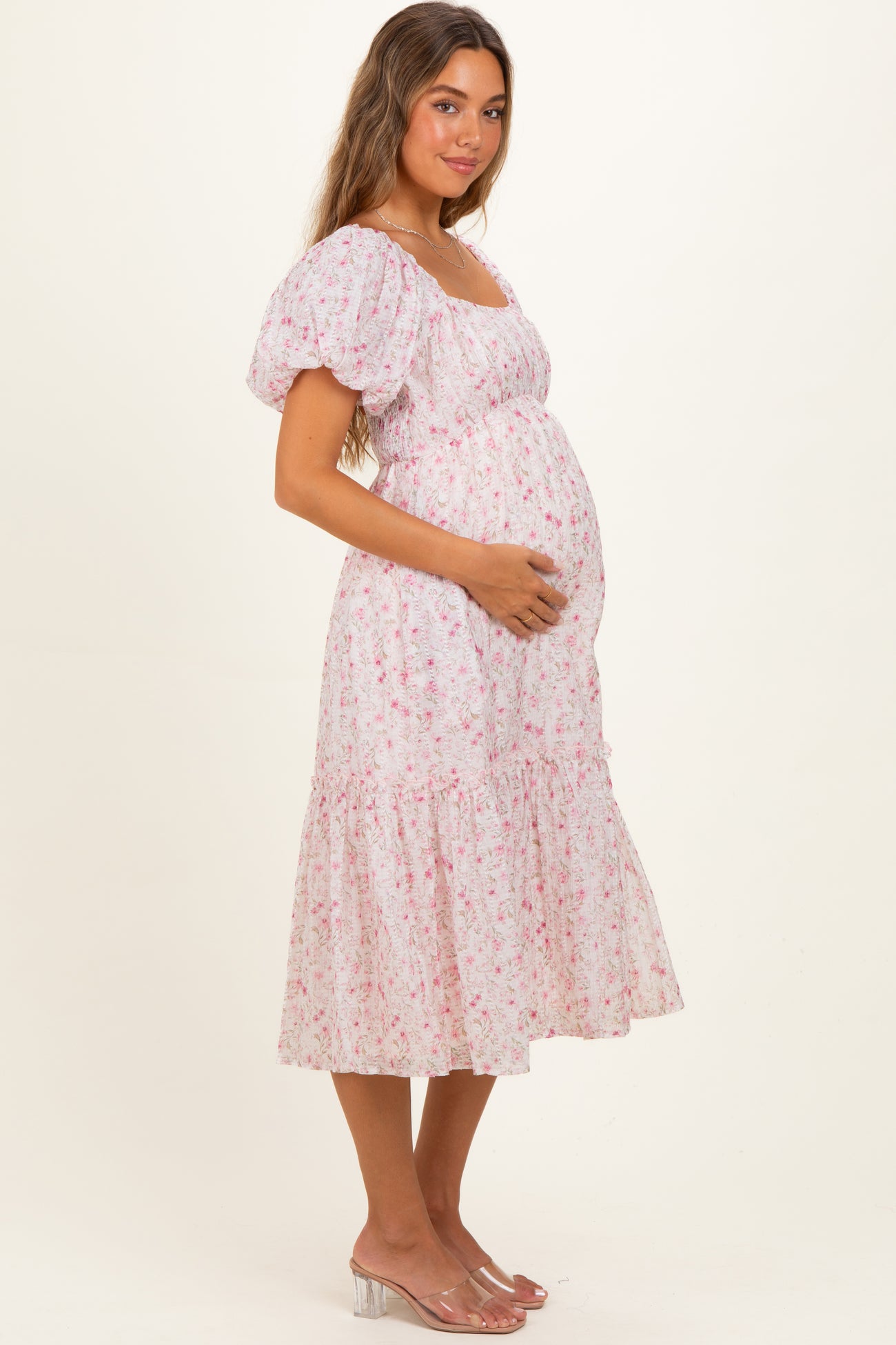 woman wearing a pink floral maternity dress with puff sleeves and holding her baby bump