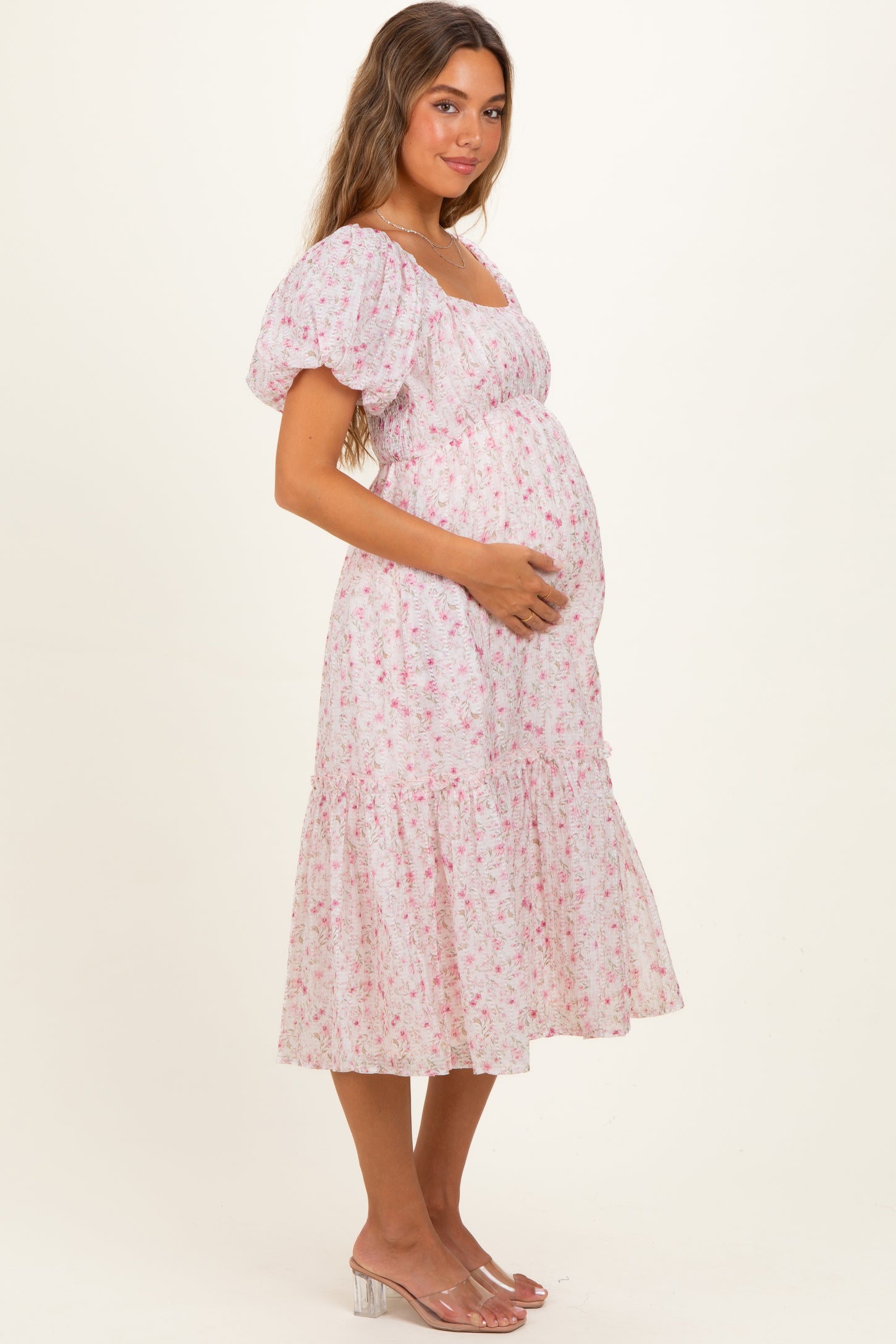 woman wearing a pink floral maternity dress with puff sleeves and holding her baby bump