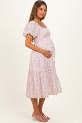 woman wearing a pink floral maternity dress with puff sleeves and holding her baby bump