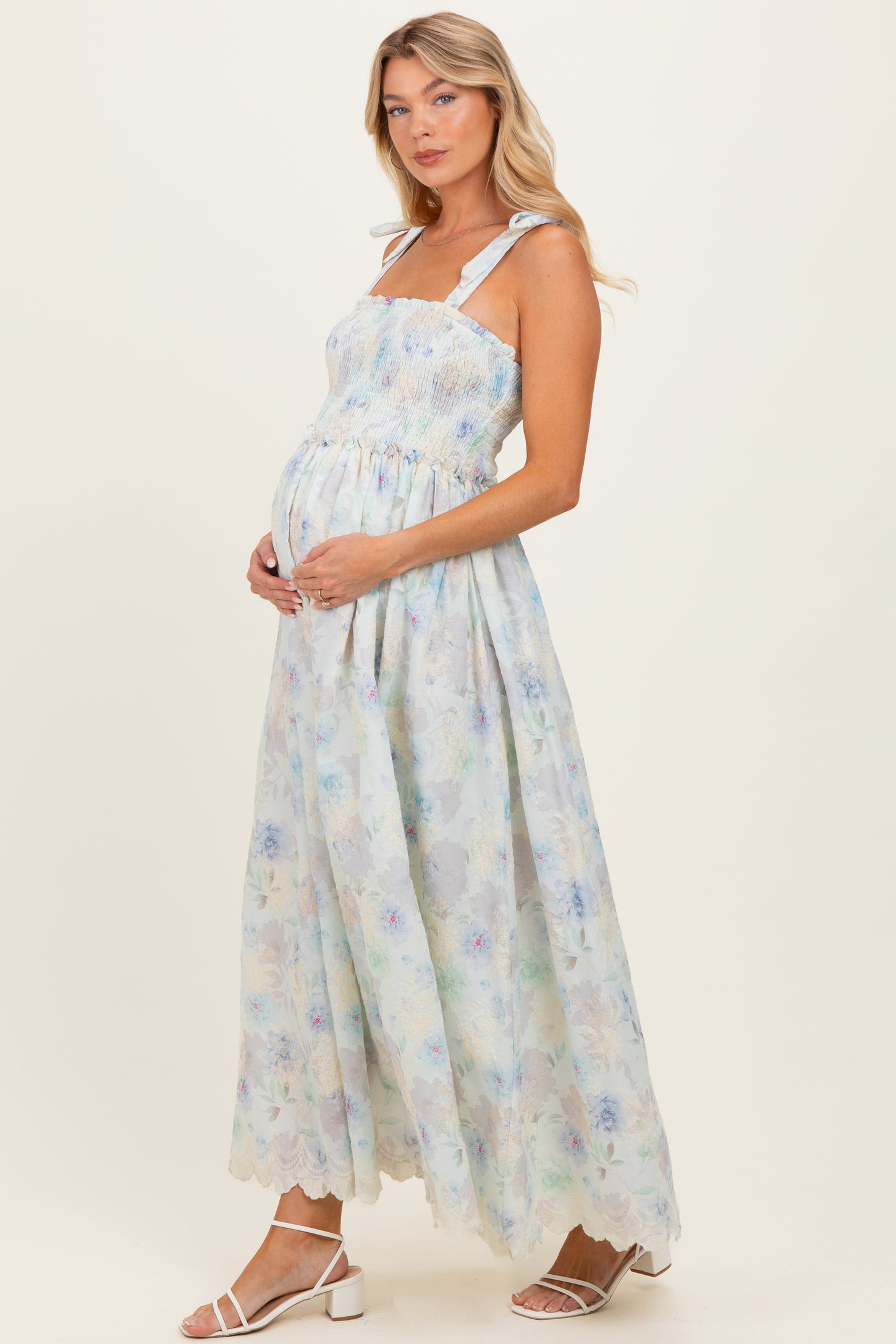 woman wearing a floral maternity maxi dress with smocked bodice and wide straps, cradling her baby bump