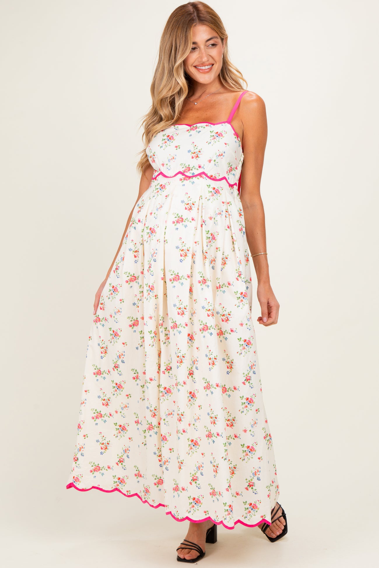 woman wearing a floral maternity maxi dress with pink trim and spaghetti straps, showcasing her baby bump