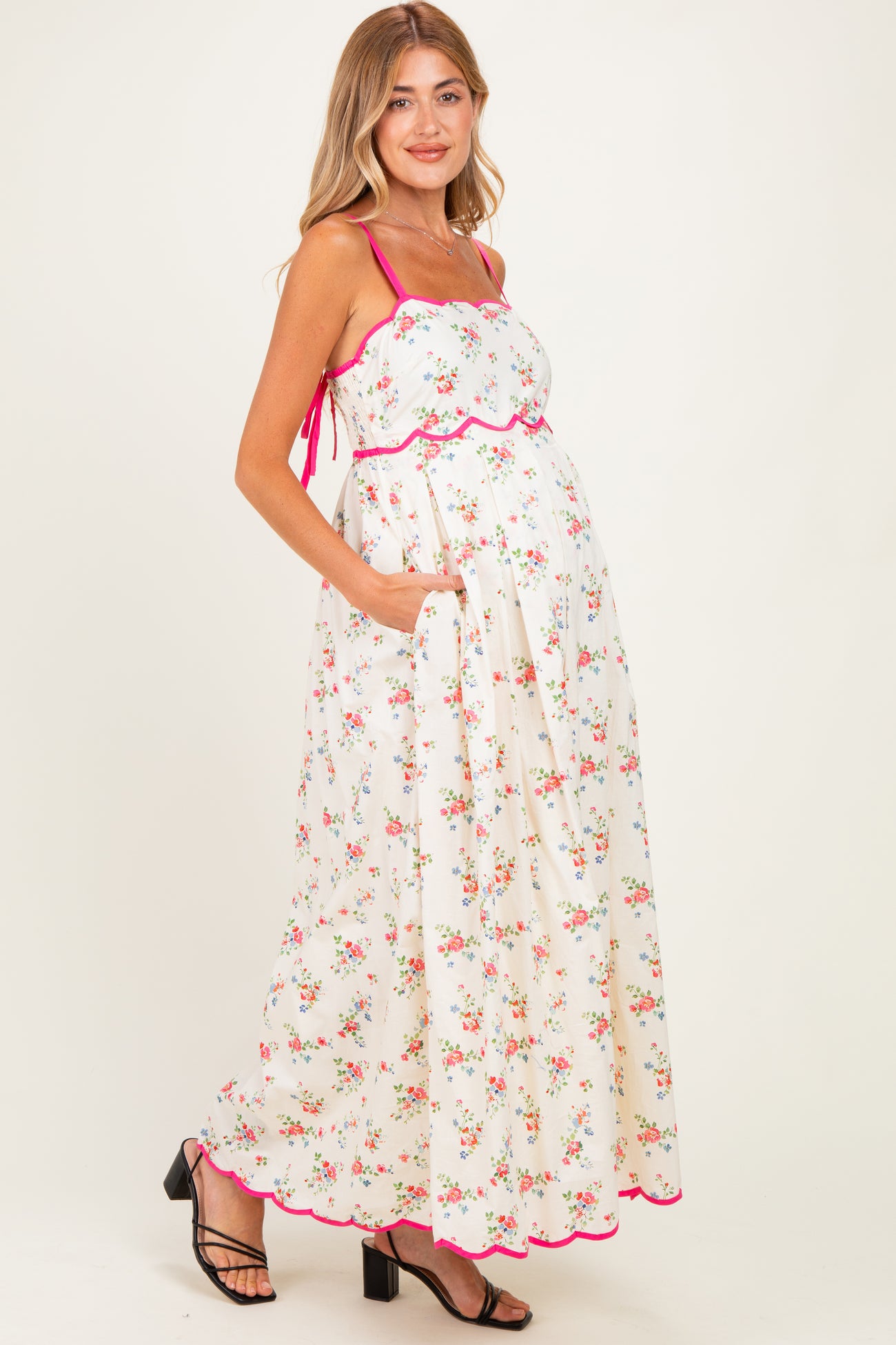 woman wearing a floral print maternity maxi dress with spaghetti straps and pockets, showing a baby bump