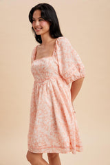 woman wearing a light peach floral print puff sleeve dress with a square neckline and gathered waist