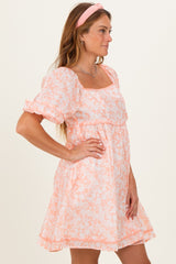 woman wearing a short pink floral dress with puff sleeves and a square neckline, styled with a headband