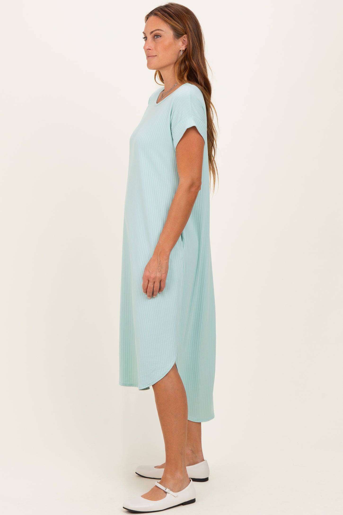 woman wearing a light green ribbed midi dress with short sleeves and side slits, standing sideways on a plain background
