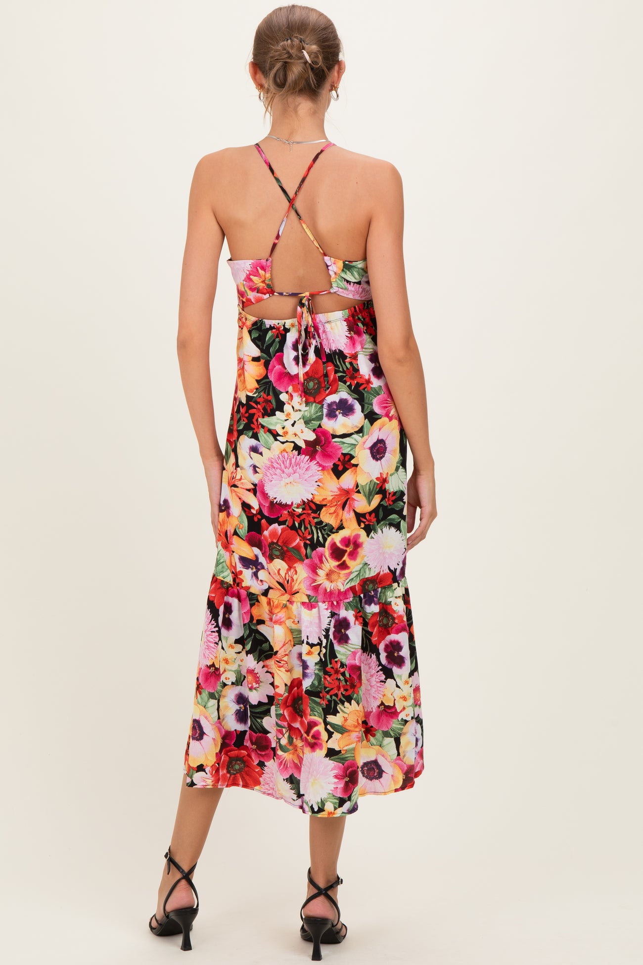 woman wearing a floral print maternity dress with cross-back straps and a tied detail at the back, showing a baby bump