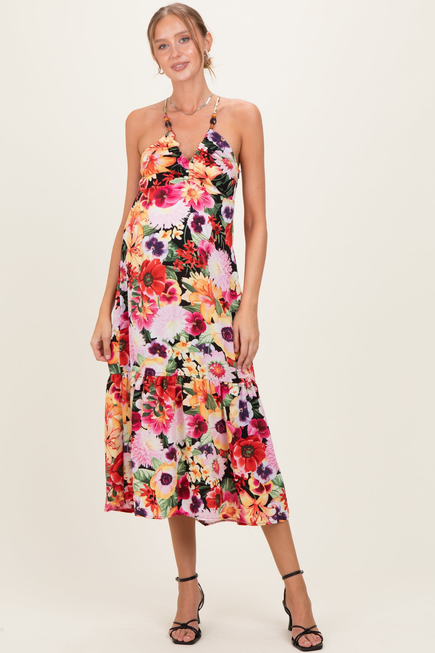 woman wearing a floral maternity dress with a halter neckline and tiered skirt, highlighting her baby bump