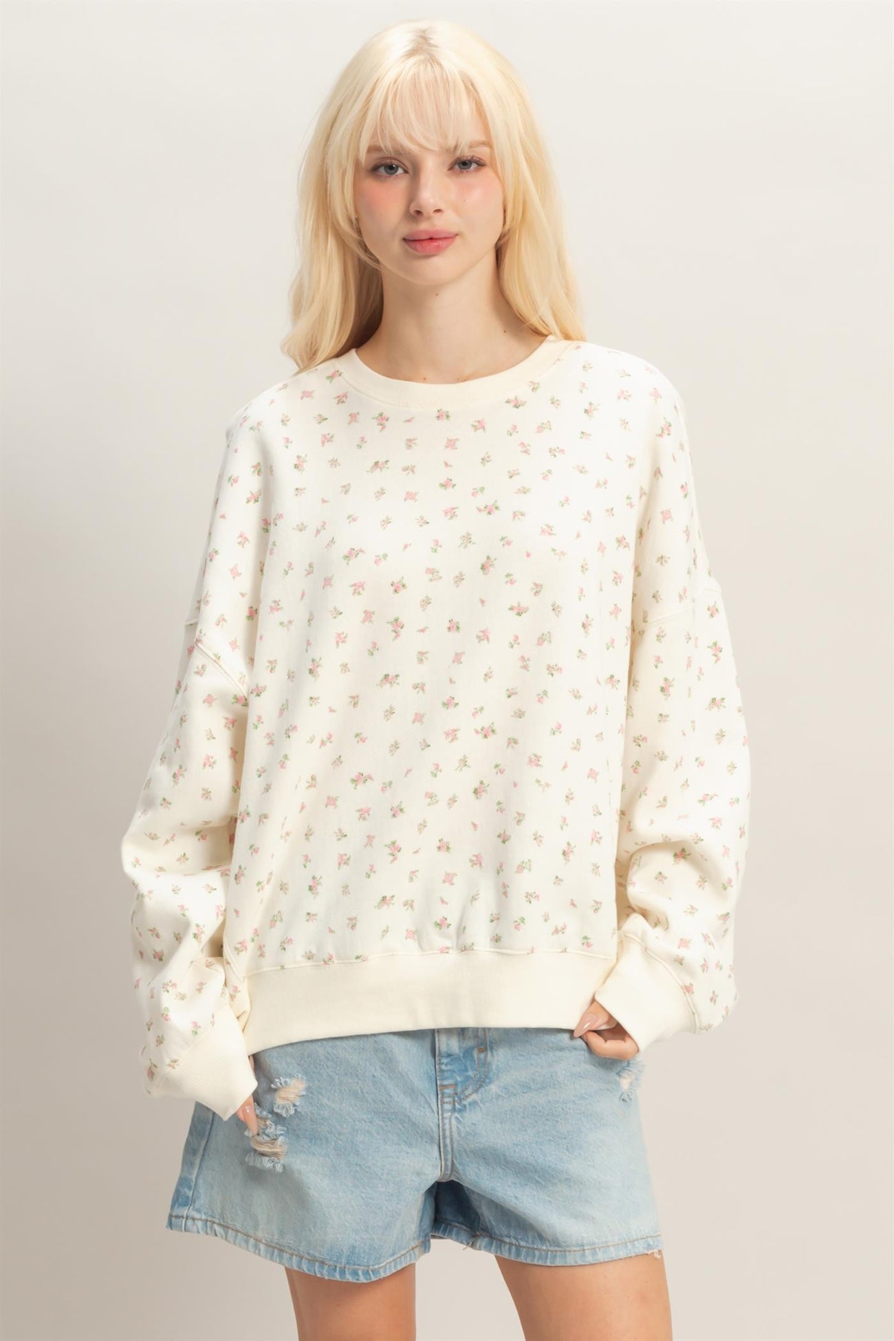 woman wearing a cream floral print oversized sweatshirt with long sleeves and distressed denim shorts