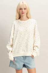 woman wearing a cream floral print oversized sweatshirt with long sleeves and distressed denim shorts