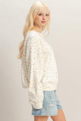 woman wearing a cream oversized sweatshirt with small floral print and paired with distressed denim shorts