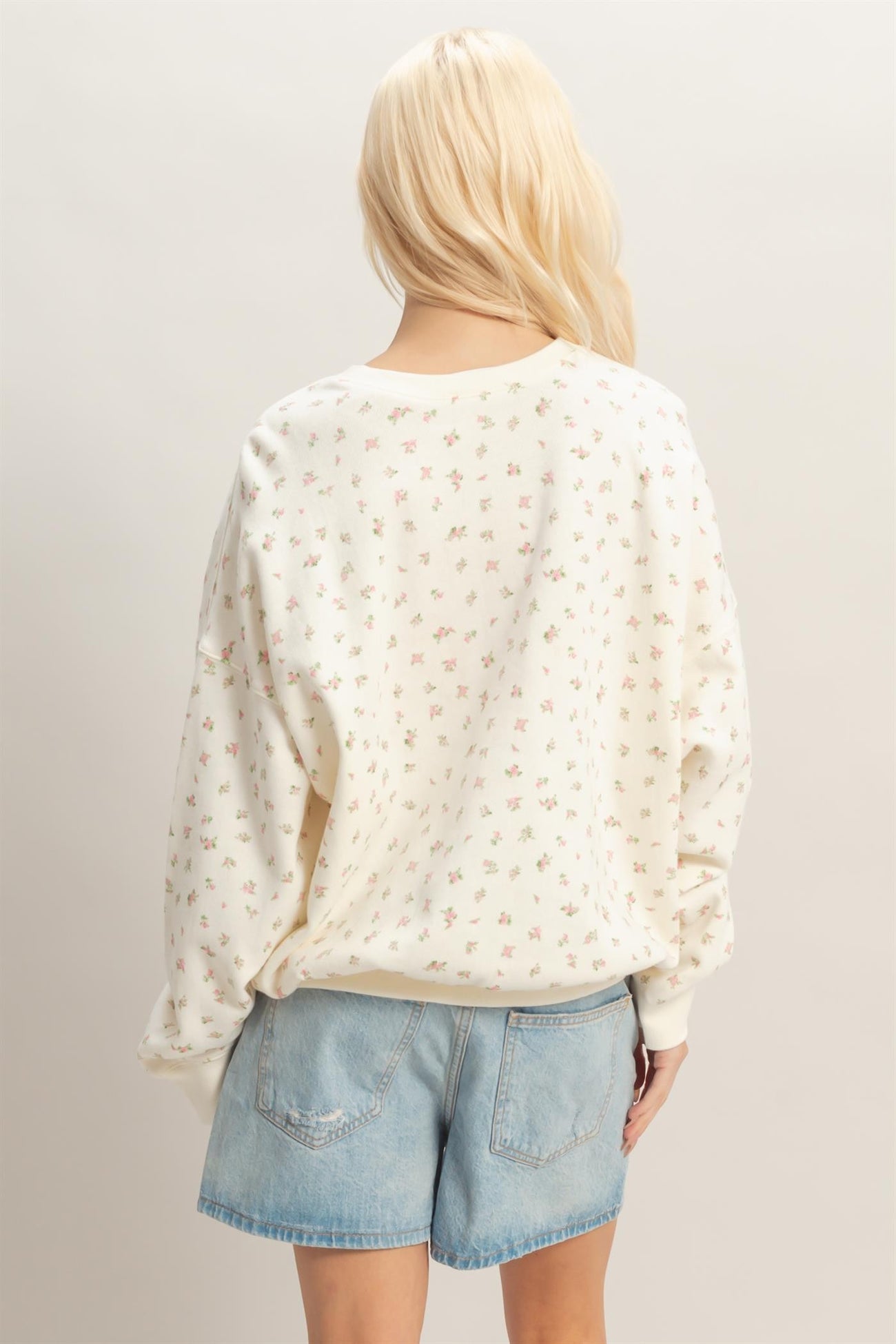 woman wearing a cream floral print oversized sweatshirt with long sleeves and light blue denim shorts