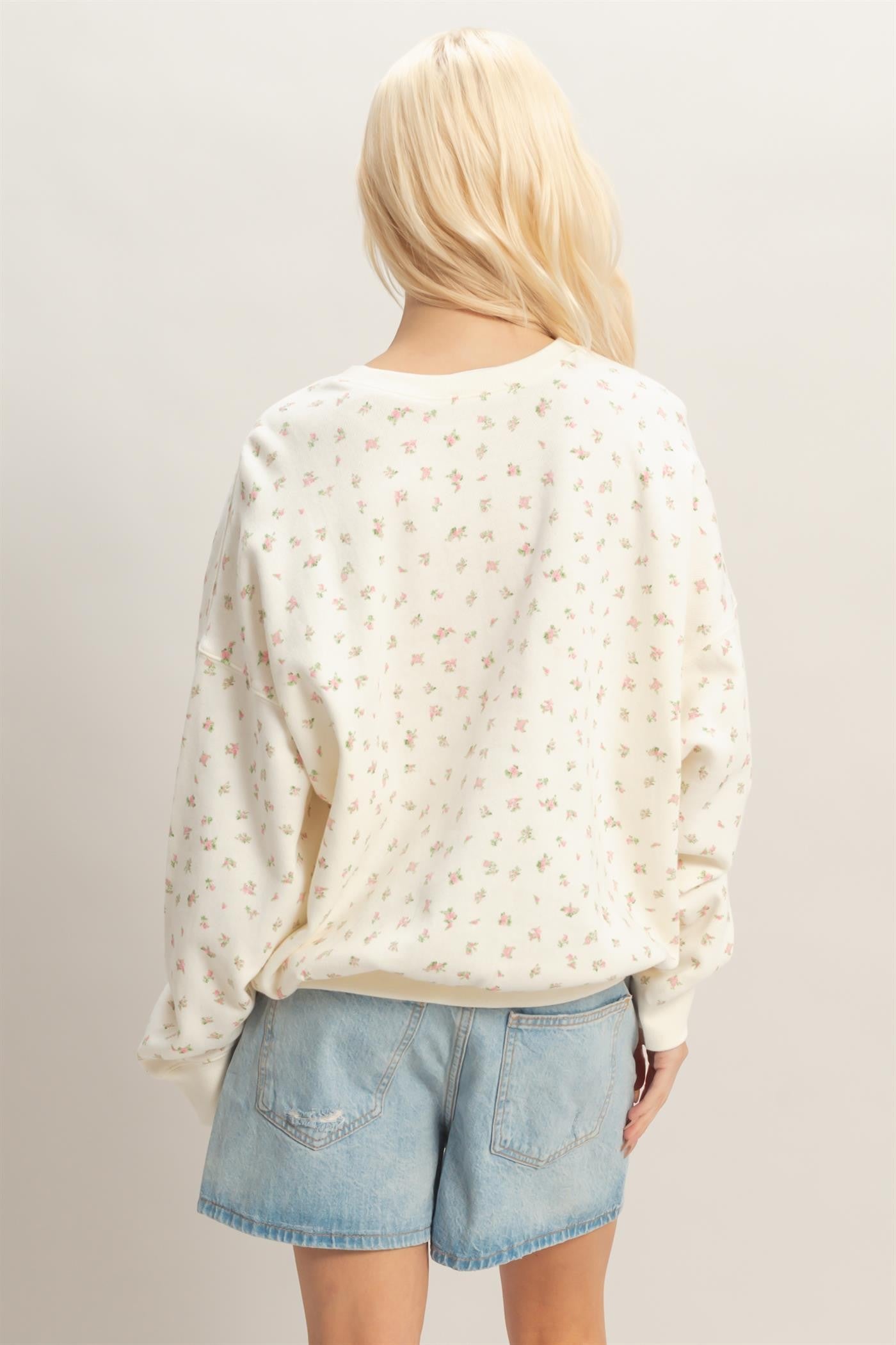 woman wearing a cream floral print oversized sweatshirt with long sleeves and light blue denim shorts
