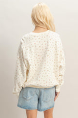 woman wearing a cream floral print oversized sweatshirt with long sleeves and light blue denim shorts