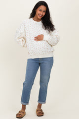 woman wearing a cream floral maternity sweatshirt and blue rolled-up jeans, holding her baby bump
