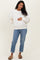 woman wearing a cream floral maternity sweatshirt and blue rolled-up jeans, holding her baby bump
