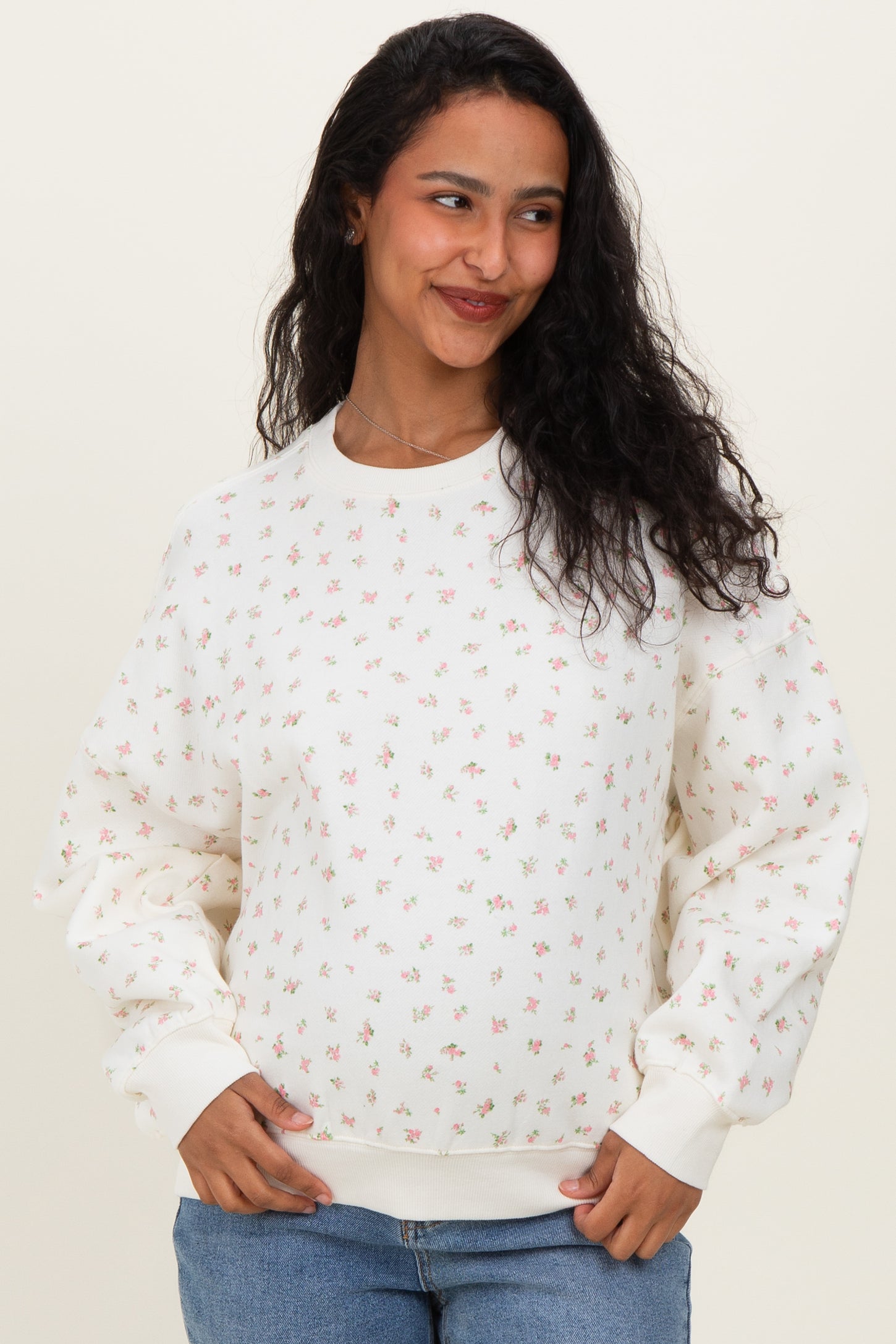 woman wearing a cream maternity sweatshirt with a floral print and a visible baby bump