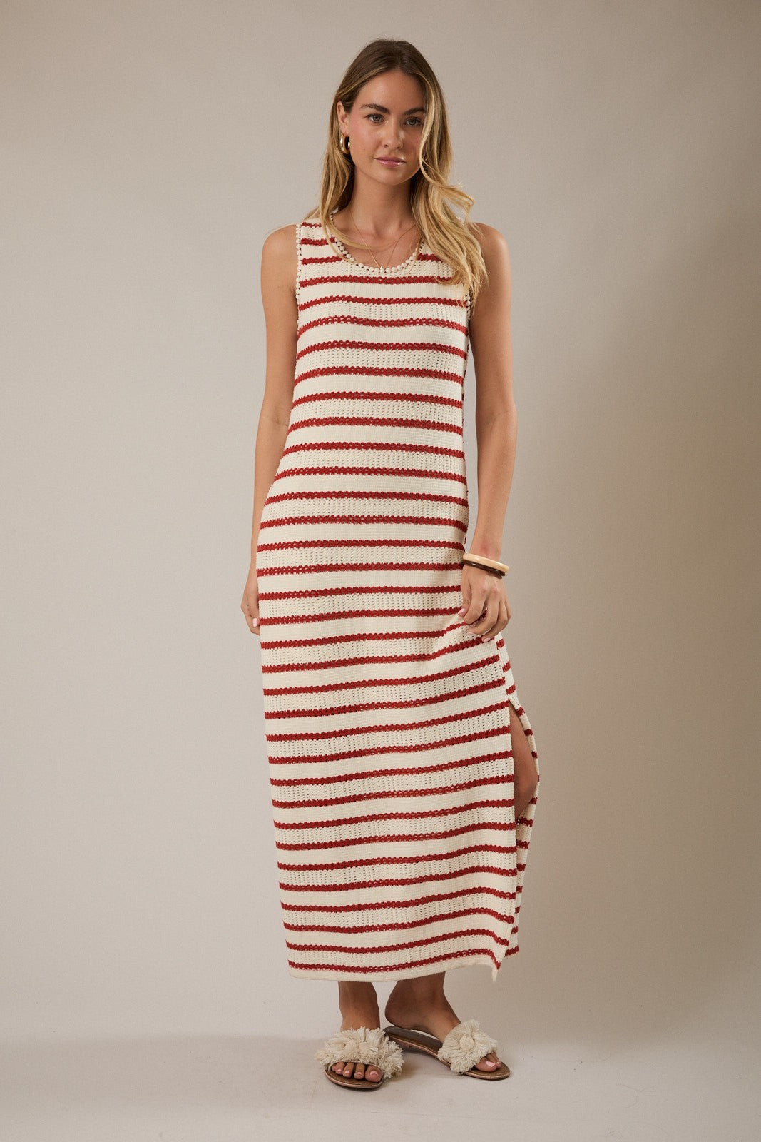 woman wearing a sleeveless cream and red striped maxi dress with side slits and sandals