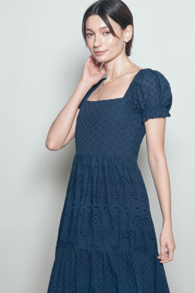 woman wearing a navy blue puff sleeve midi dress with a tiered skirt and embroidered details