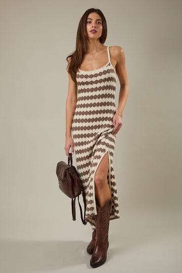 woman wearing a beige and brown patterned maxi dress with a side slit and brown cowboy boots, posing with a brown handbag