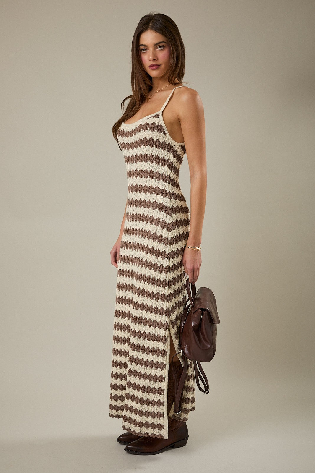 woman wearing a cream and brown patterned spaghetti strap maxi dress with side slits and holding a brown bag