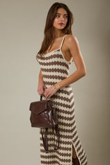 woman wearing a beige and brown patterned maxi dress with side slits, holding a brown backpack purse