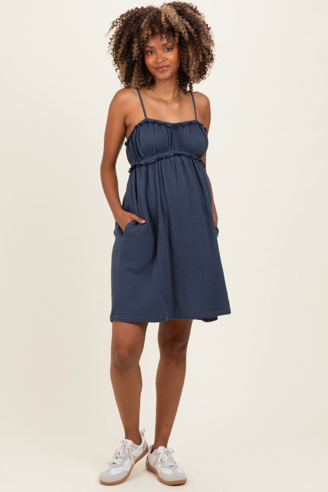 woman wearing a navy blue maternity dress with adjustable straps and pockets, showcasing her baby bump