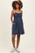 woman wearing a navy blue maternity dress with adjustable straps and pockets, showcasing her baby bump