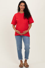 woman wearing a red short sleeve maternity top and holding her baby bump, paired with light blue jeans and sandals