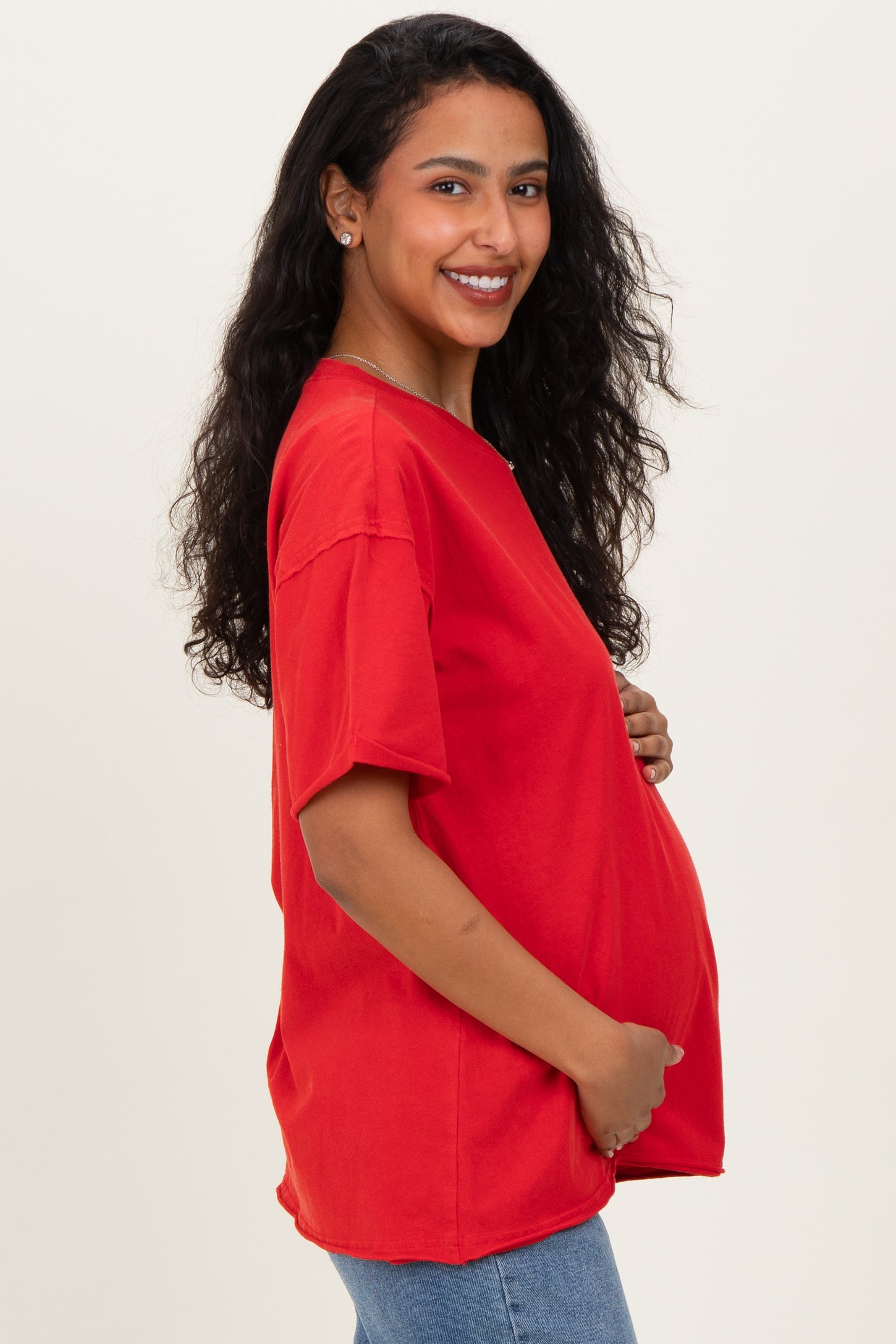 woman wearing a red oversized maternity t-shirt and cradling her baby bump