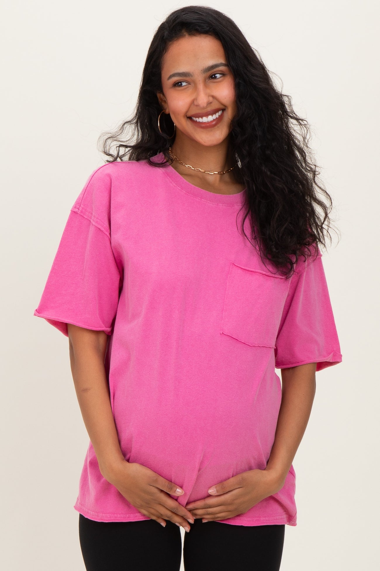 woman wearing a bright pink short sleeve maternity t-shirt with a pocket, holding her baby bump
