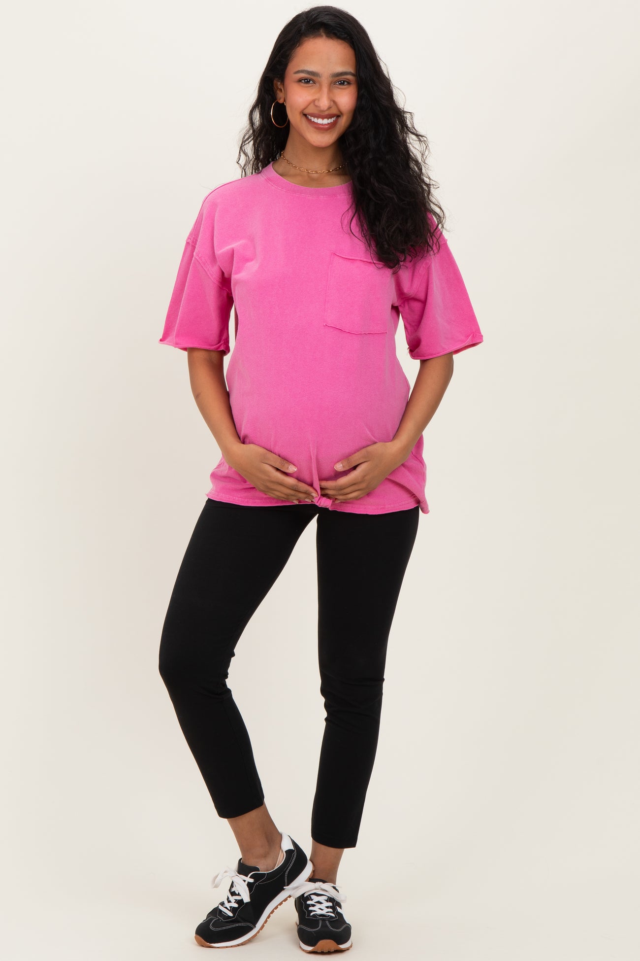 woman wearing a bright pink maternity t-shirt with a pocket and black leggings, holding her baby bump