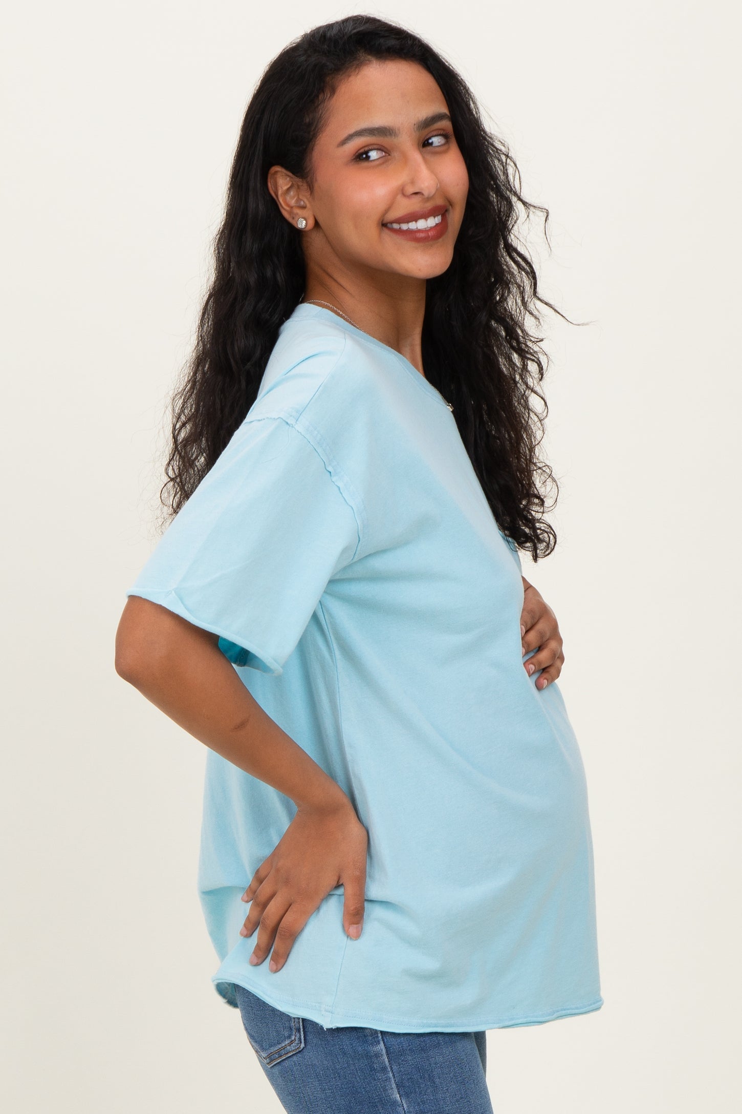 woman wearing a light blue oversized maternity t-shirt and holding her baby bump