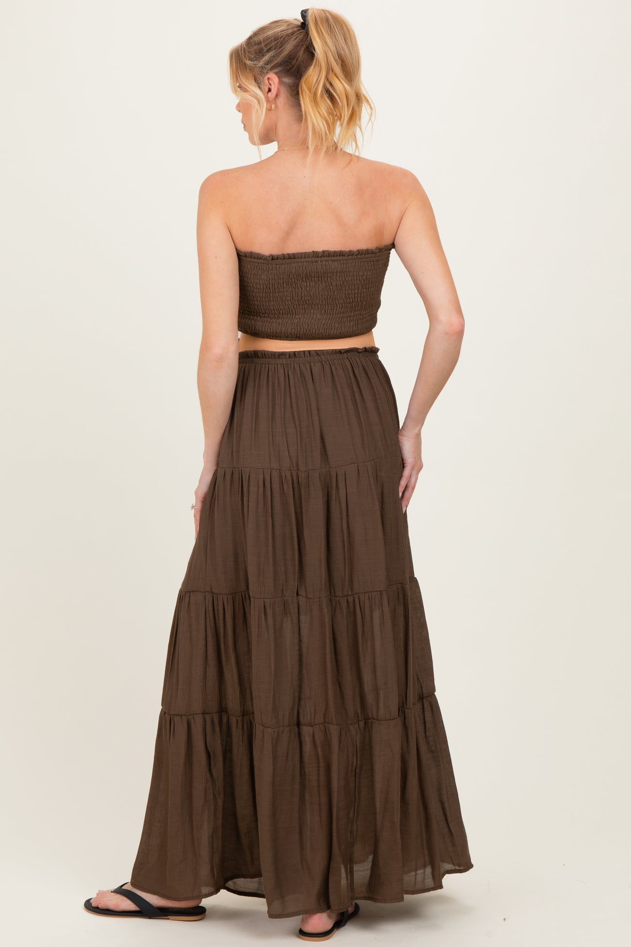 woman wearing a brown strapless maternity dress with a smocked bodice and tiered maxi skirt, showing back view
