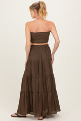 woman wearing a brown strapless maternity dress with a smocked bodice and tiered maxi skirt, showing back view