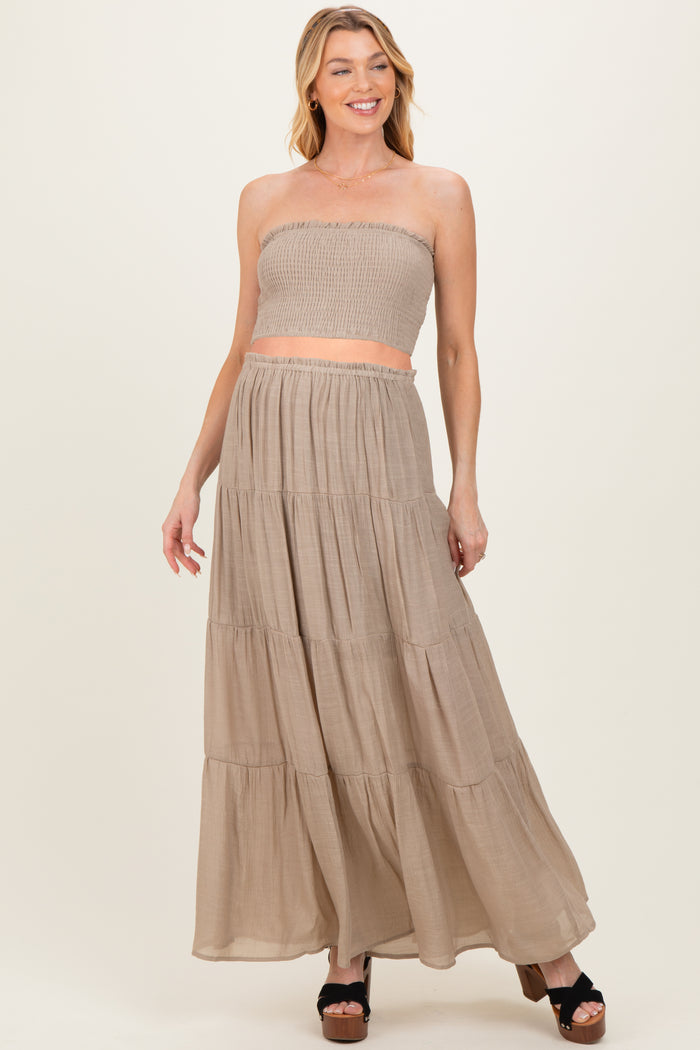 woman wearing a beige strapless smocked maternity crop top and matching maxi skirt, smiling with hands on hips