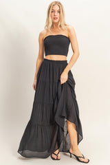woman wearing a black smocked crop top and a black tiered maxi skirt with a high-low hemline and heeled sandals