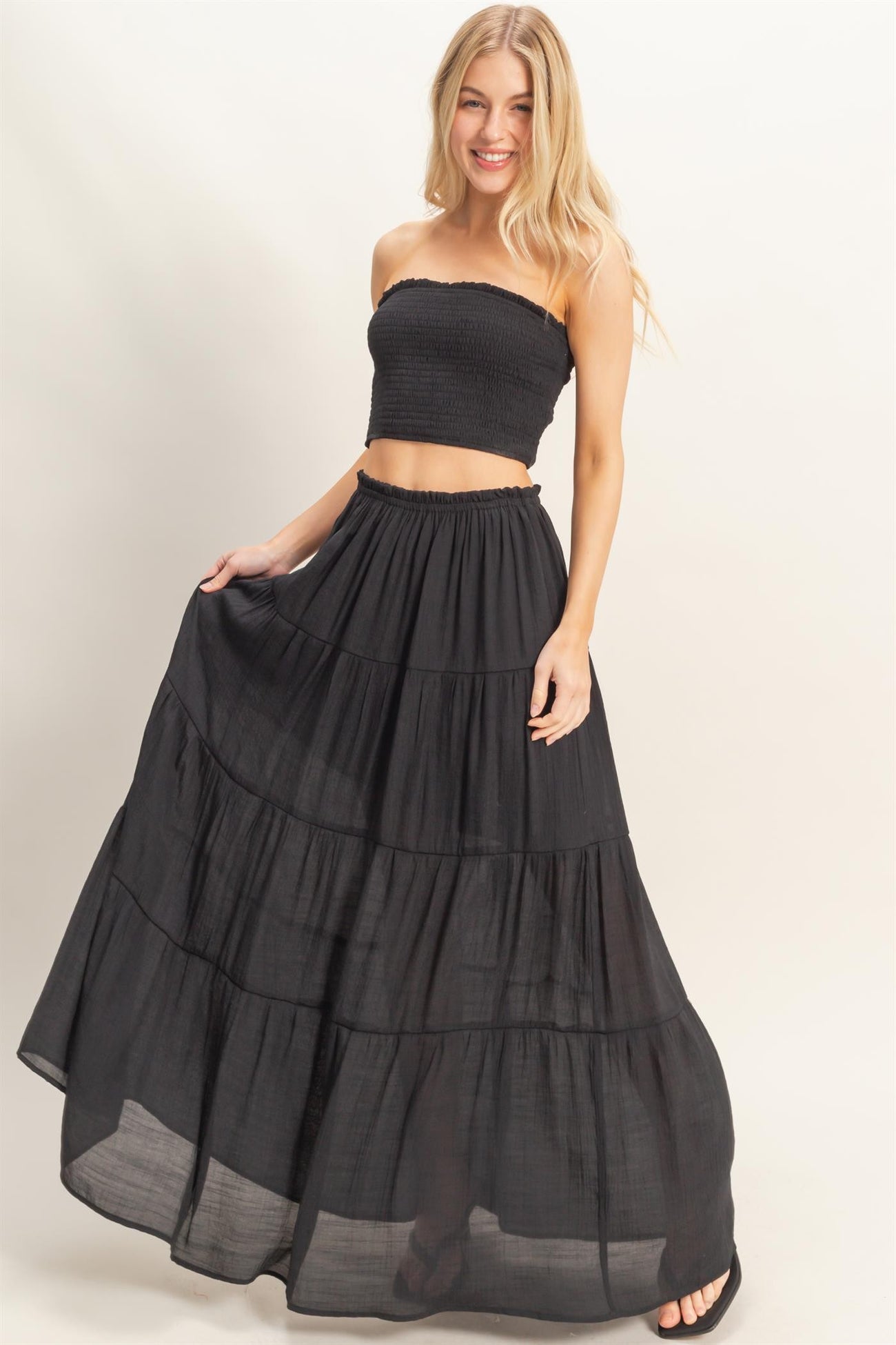 woman wearing a black smocked crop top and a flowy black tiered maxi skirt