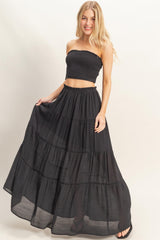 woman wearing a black smocked crop top and a flowy black tiered maxi skirt