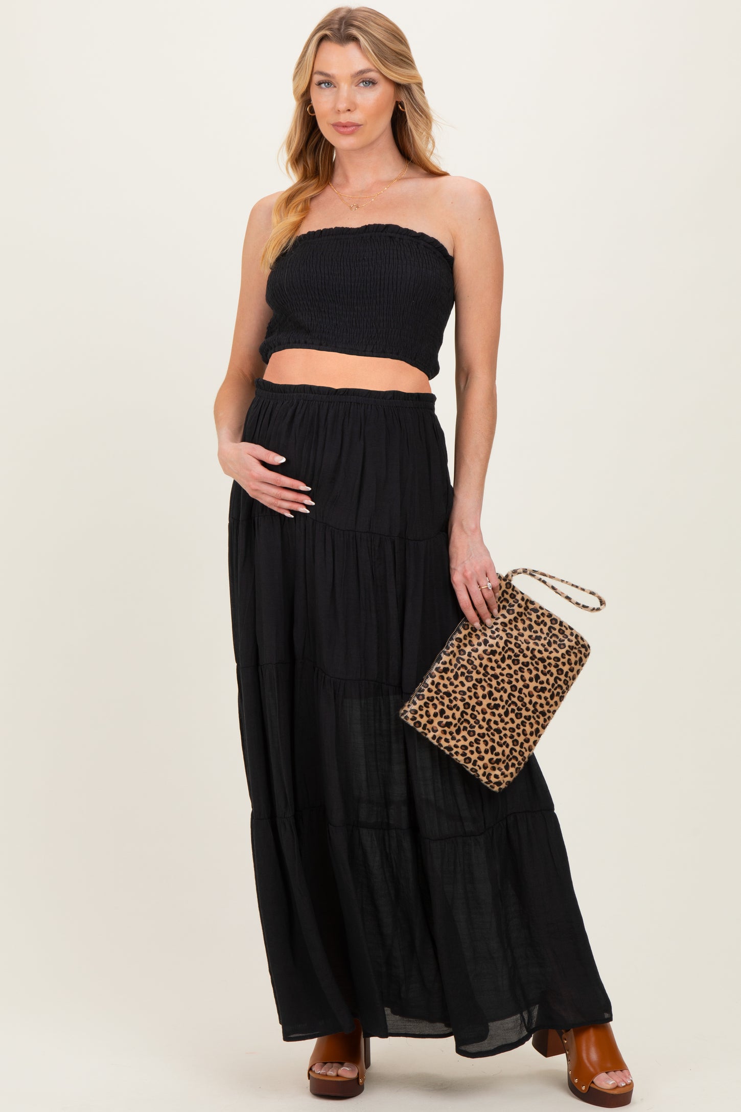 woman wearing a black strapless maternity top and a flowing black tiered maxi skirt, holding a leopard print clutch and showing her baby bump