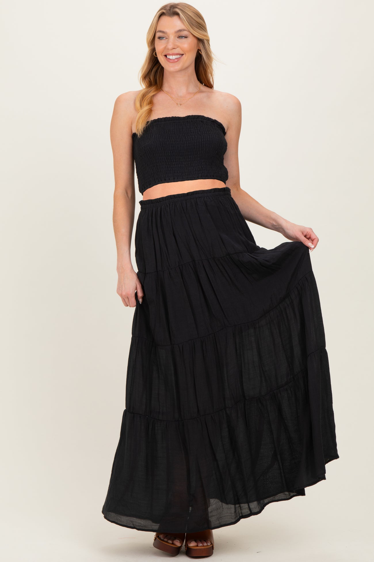 woman wearing a black strapless smocked crop top and a flowing black maxi skirt, showcasing her baby bump