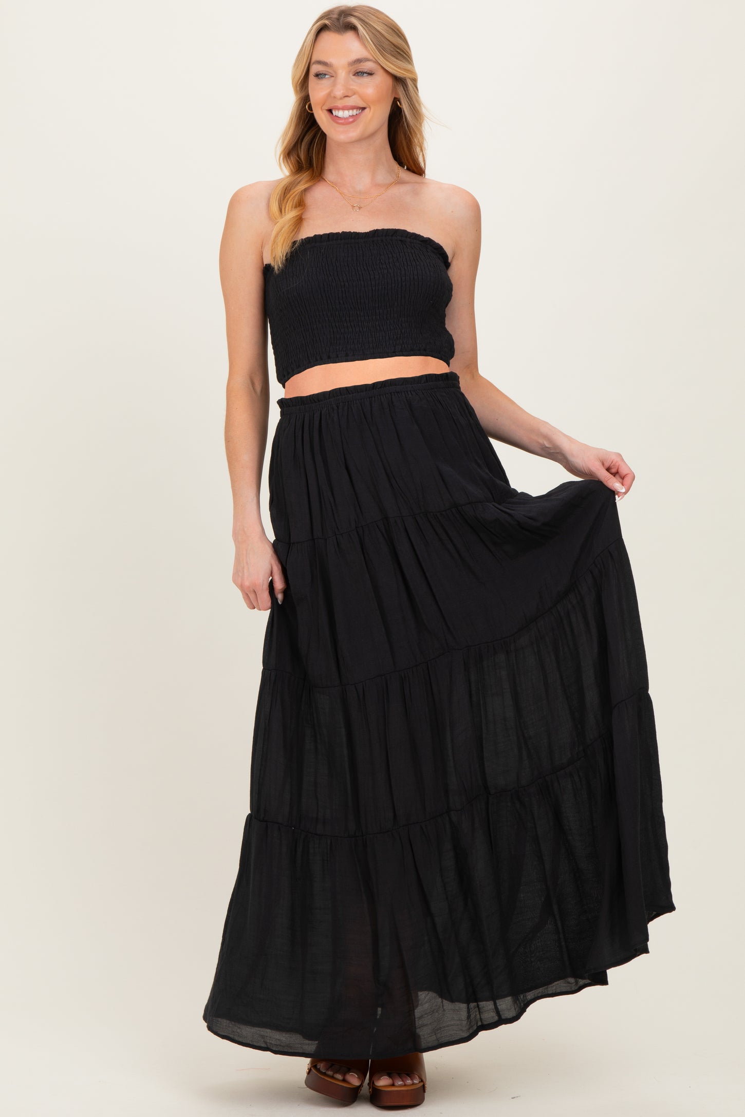 woman wearing a black strapless smocked crop top and a flowing black maxi skirt, showcasing her baby bump