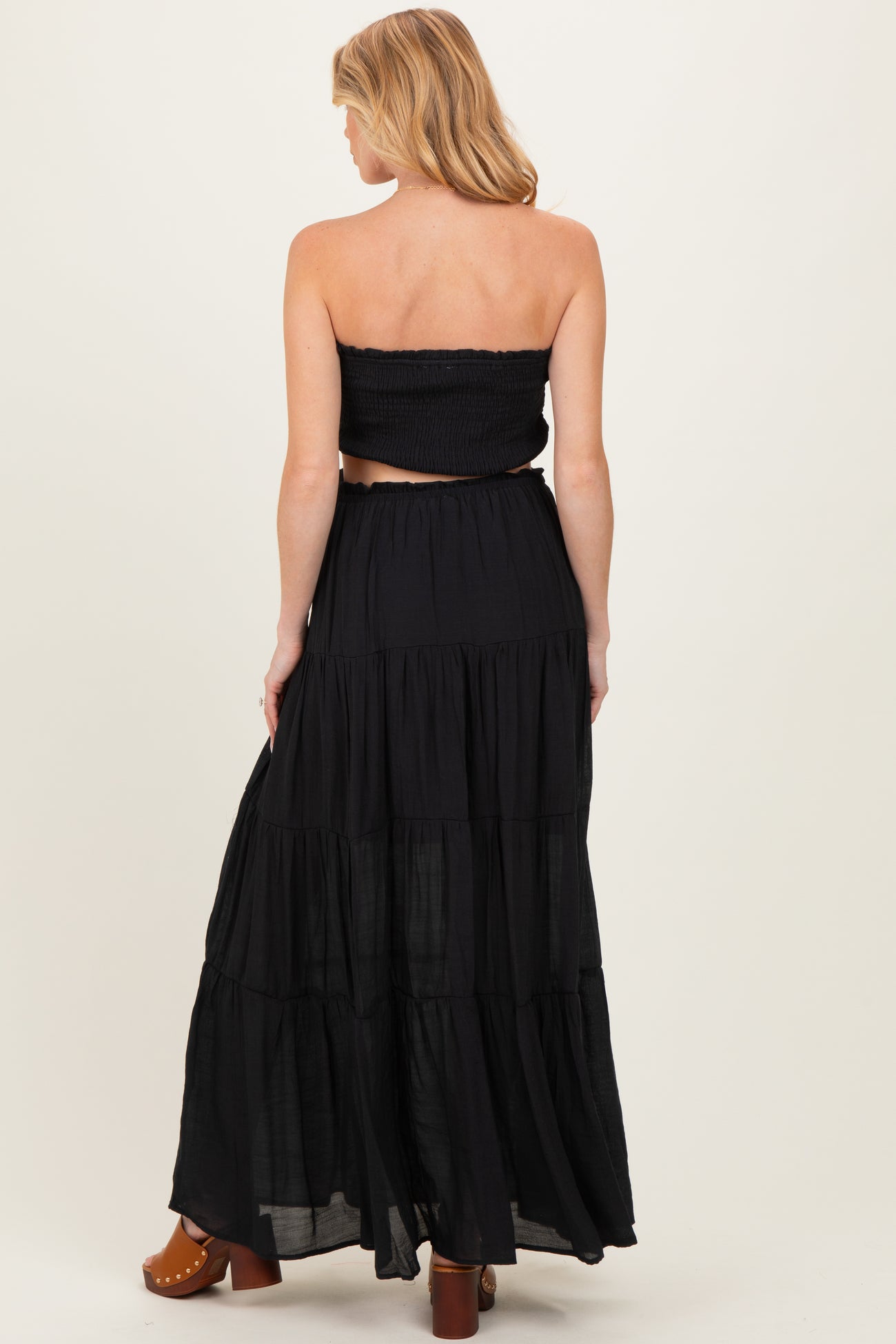 woman wearing a black maternity two-piece set with a smocked crop top and a flowing tiered maxi skirt, showing her baby bump