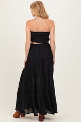 woman wearing a black maternity two-piece set with a smocked crop top and a flowing tiered maxi skirt, showing her baby bump