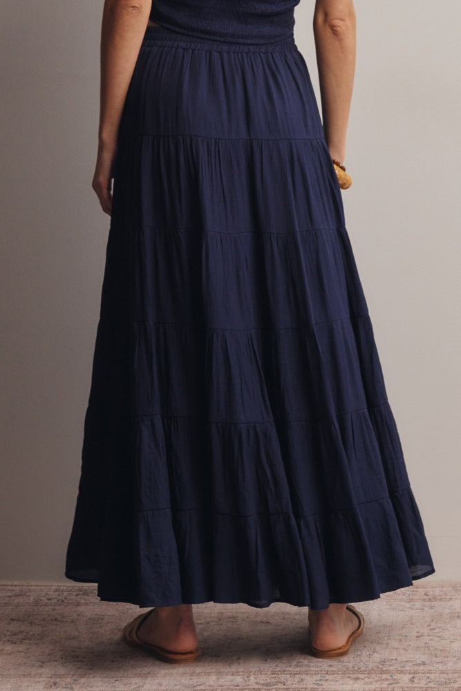woman wearing a navy blue tiered maxi skirt, viewed from the back, with a flowy design and elastic waistband