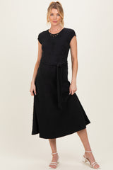 woman wearing a black maternity dress with a fitted top and a flowy skirt, accessorized with a belt and standing confidently