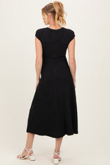 woman wearing a black cap sleeve maternity dress with a flowy midi length and floral texture, shown from the back