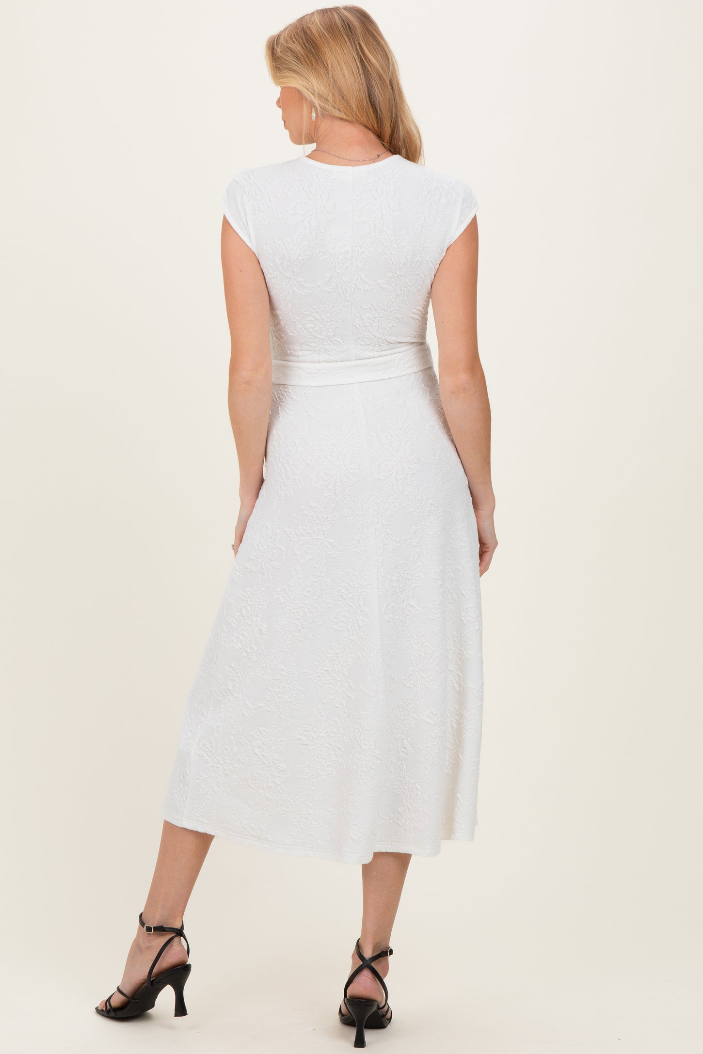 woman wearing a white maternity dress with cap sleeves and a belted waist, showing a baby bump from the back