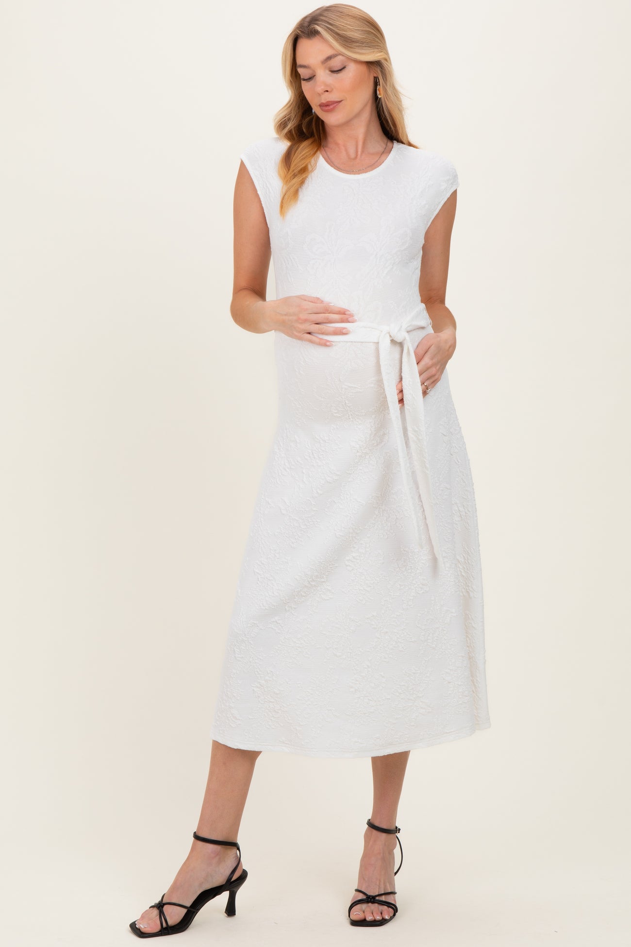 woman wearing a white sleeveless maternity dress with a tie waist and a visible baby bump