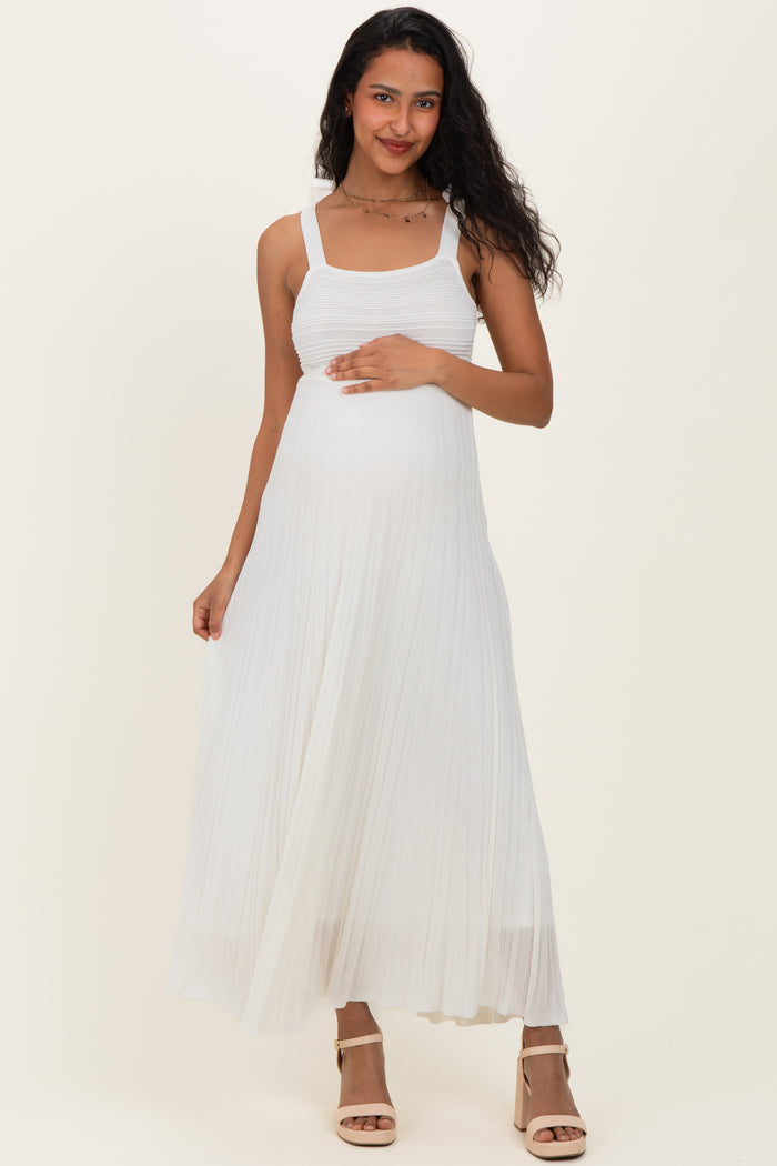 woman wearing a white pleated maternity dress and gently holding her baby bump